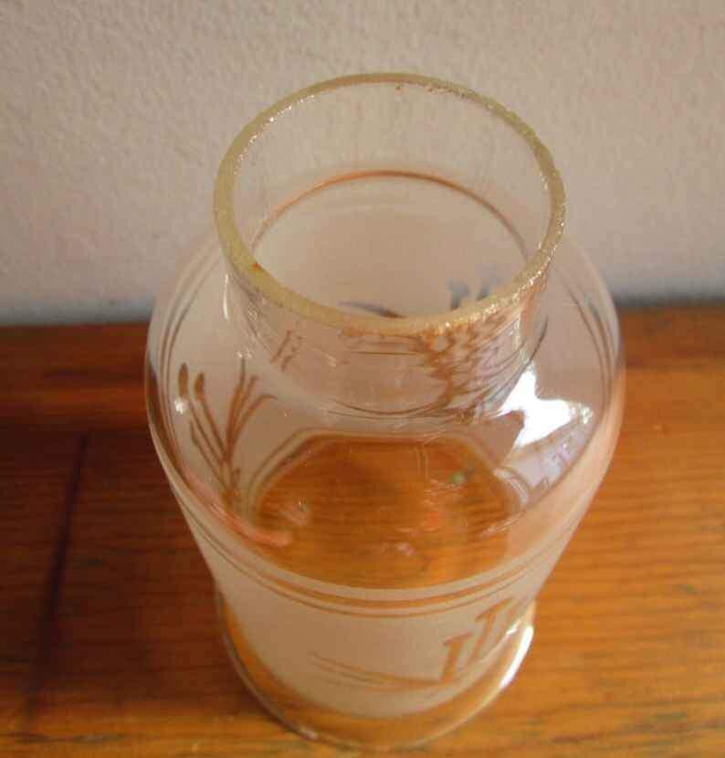 May include: A clear glass bottle with a frosted finish and a decorative design. The bottle has a wide mouth and a rounded bottom.
