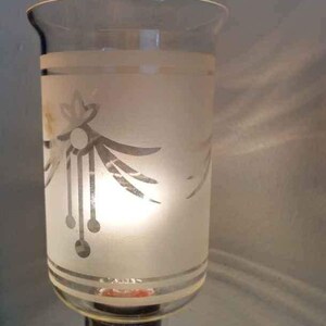 May include: A frosted glass lampshade with a silver etched design of a stylised flower and leaves. The lampshade is clear at the top and bottom, revealing the light bulb inside.