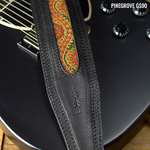 May include: Black leather guitar strap with a paisley patterned fabric insert. The strap has a stitched design and a small logo on the front.
