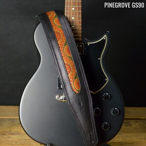 May include: A black electric guitar with a black leather guitar strap with an orange and green paisley design. The strap is labeled "Pinegrove GS90".
