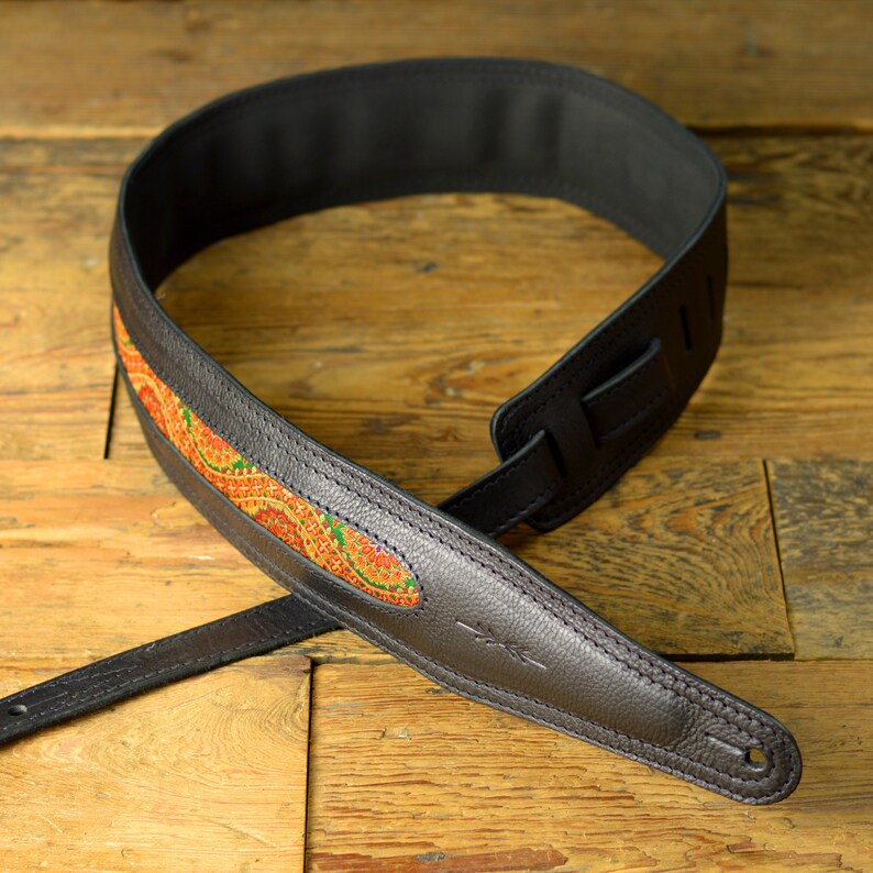 May include: Black leather guitar strap with a colorful patterned inlay. The strap is designed for comfort and durability.