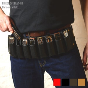 Pode incluir: Um cinto de couro preto para gaita com oito ranhuras para gaitas. O cinto é usado por uma pessoa e tem uma fivela de couro marrom. O texto "PINEGROVE LEATHER Harmonica Belt" é visível no cinto.
