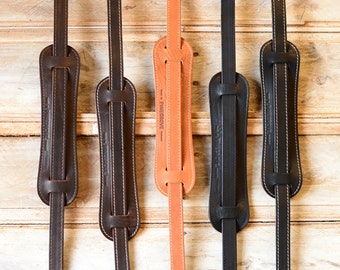 May include: Four leather guitar straps in different colors: brown, black, tan, and black. The straps have a stitched design and the text "PINEGROVE" is visible on the tan strap. The text "PINEGROVE GS25" is visible at the bottom of the image.