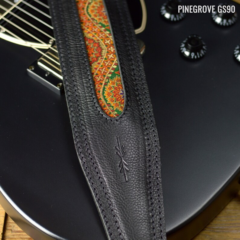 May include: Black leather guitar strap with a paisley patterned fabric insert. The strap has a stitched design and a small logo on the front.