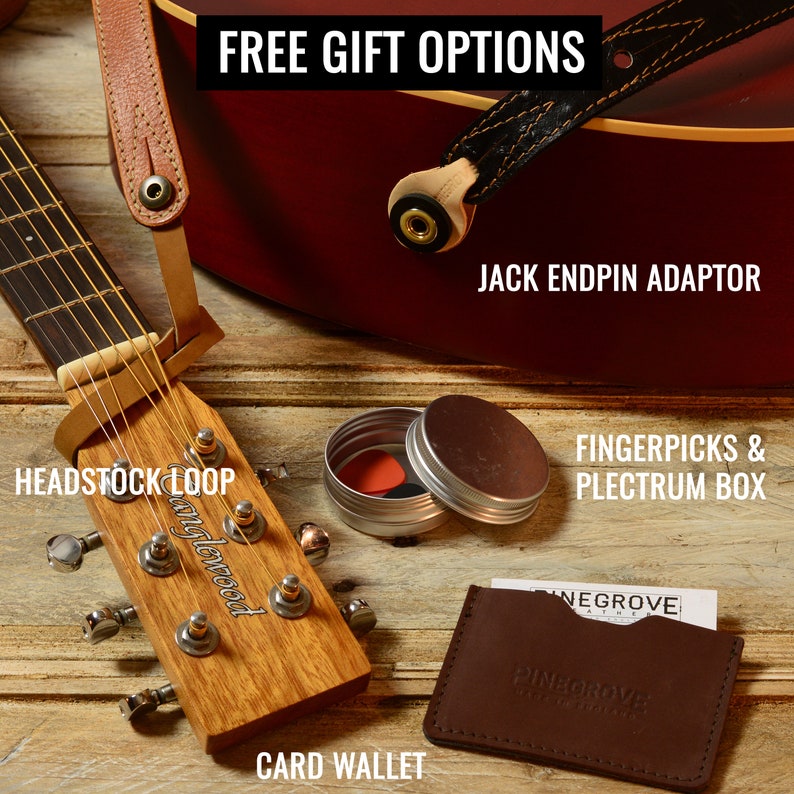 May include: A close-up of a wooden guitar headstock with a brown leather strap, a small tin with fingerpicks, a brown leather card wallet, and a brown leather guitar strap with a black endpin adaptor. The text "FREE GIFT OPTIONS", "HEADSTOCK LOOP", "anglewood", "JACK ENDPIN ADAPTOR", "FINGERPICKS & PLECTRUM BOX", "CARD WALLET", "NEGROVE", and "PINAGROVE" is visible in the image.