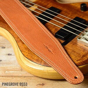 May include: A brown leather guitar strap with white stitching and a small arrow design. PINEGROVE BS53 is printed on the bottom of the image.