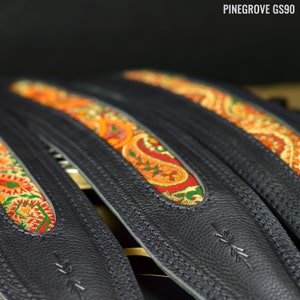 May include: Three black leather guitar straps with colorful paisley patterned fabric inserts. The straps are stitched with white thread and have a small logo on the bottom.