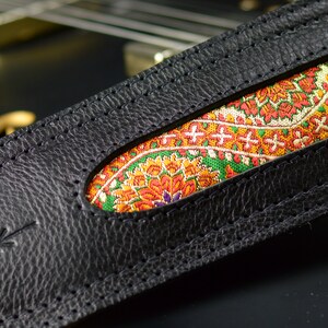 May include: Black leather guitar strap with a colorful paisley pattern insert. The strap has a stitched edge.