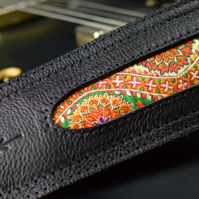 May include: Black leather guitar strap with a colorful paisley pattern insert. The strap has a stitched edge.