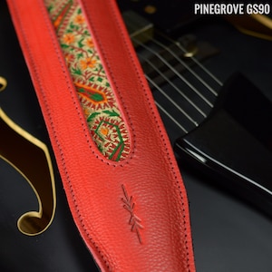 Könnte beinhalten: Roter Gitarrengurt aus Leder mit einem bunten Stickmuster und einem gestickten Pfeildetail. PINEGROVE GS90.