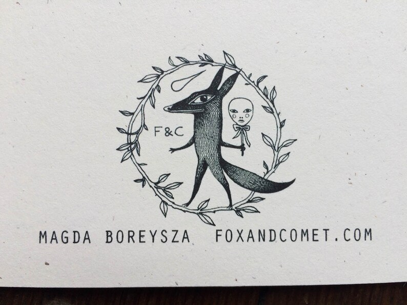 Pu&ograve; includere: Illustrazione in bianco e nero di una volpe che tiene una bambola con un cerchio di foglie intorno a loro. Il testo "F&C" e "FOXANDCOMET.COM" sono anche inclusi nell'immagine.