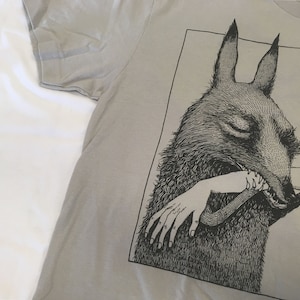 May include: A gray t-shirt with a black and white illustration of a creature with large ears biting a human arm.