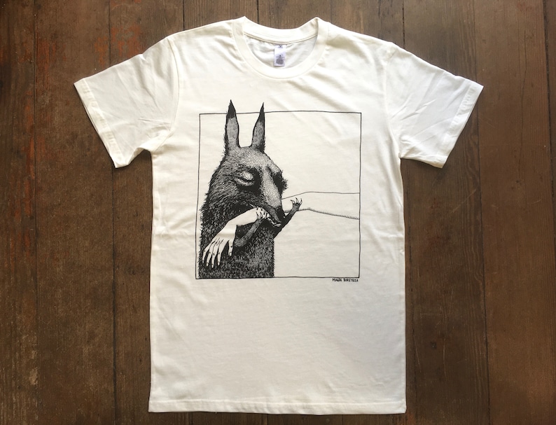 May include: White t-shirt with a black and white illustration of a creature with large ears biting a hand. The text "FRANK STELLA" is printed below the illustration.