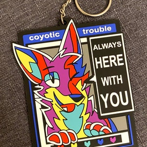 Może przedstawiać: Kolorowy kreskówkowy lis z chmurką dialogową, w której widnieje napis "Zawsze tu z Tobą". Lis znajduje się w czarnej ramce z napisem "coyotic trouble" u góry. Ramka ma niebieską obwódkę i rząd kolorowych serc na dole.