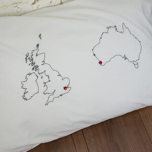 Puede incluir: Una funda de almohada blanca con contornos bordados en negro del Reino Unido y Australia. Corazones rojos est&aacute;n cosidos en el centro de cada pa&iacute;s.