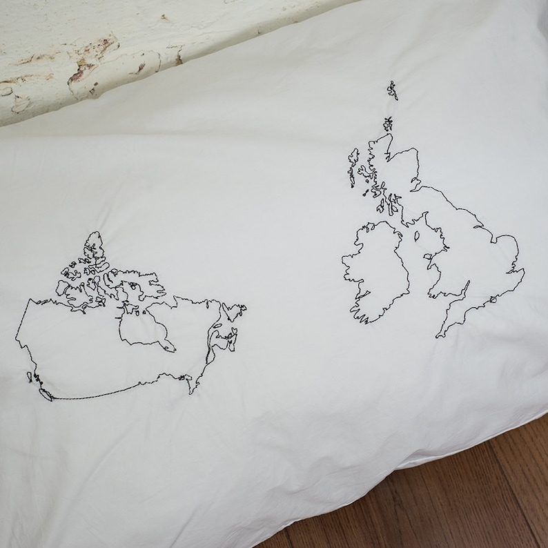 Puede incluir: Una funda de almohada blanca con contornos bordados en negro de los mapas de Canad&aacute; y el Reino Unido.