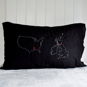 Puede incluir: Almohada negra con contornos bordados en blanco de los Estados Unidos y el Reino Unido. Alfileres rojos en forma de coraz&oacute;n marcan ubicaciones en ambos pa&iacute;ses.