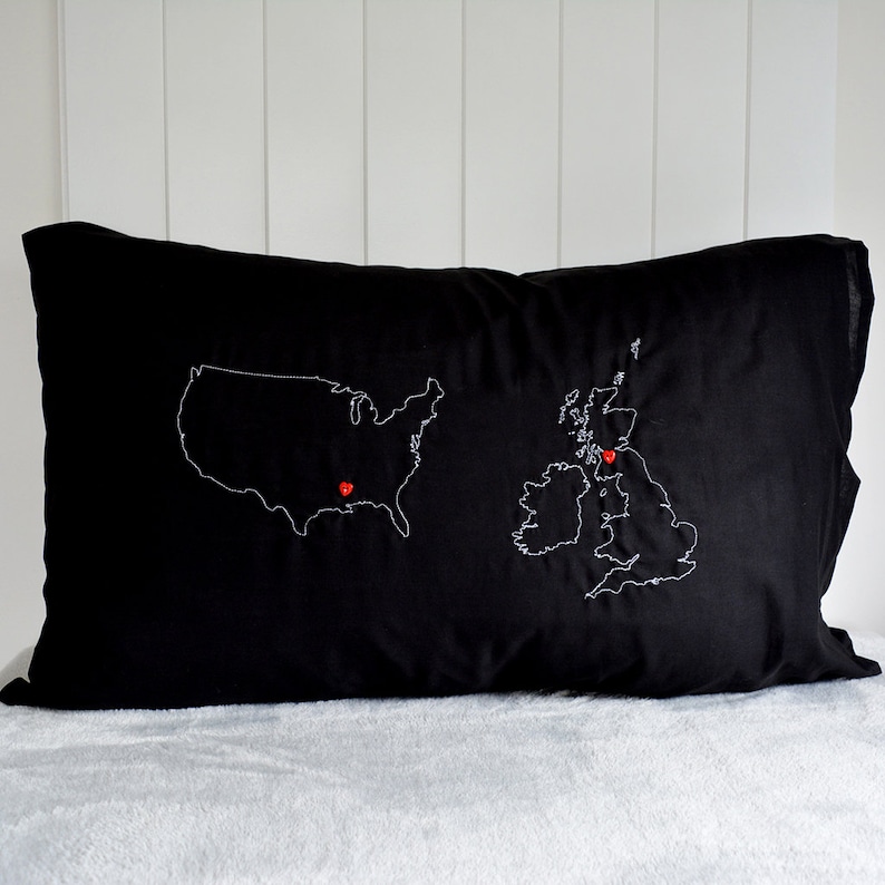 Puede incluir: Almohada negra con contornos bordados en blanco de los Estados Unidos y el Reino Unido. Alfileres rojos en forma de coraz&oacute;n marcan ubicaciones en ambos pa&iacute;ses.