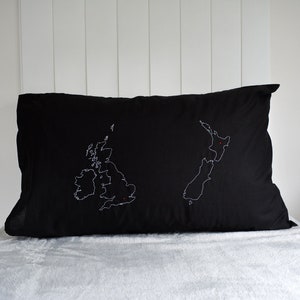 Puede incluir: Almohada negra con contornos bordados en blanco del Reino Unido y Nueva Zelanda, con puntos rojos que marcan Londres y Wellington.
