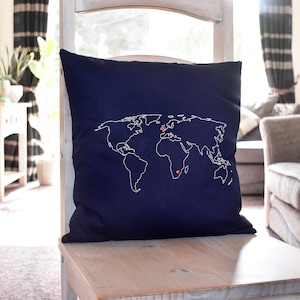 May include: A navy blue cushion with a white embroidered world map. The map has red dots marking locations on the continents.
