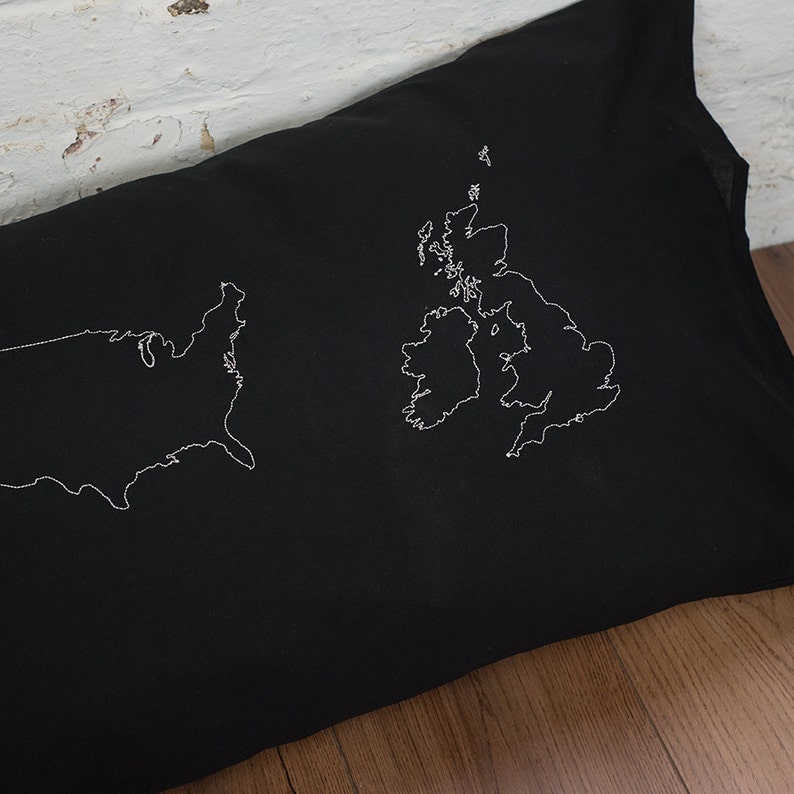 Puede incluir: Una almohada negra con contornos bordados en blanco de los Estados Unidos y el Reino Unido.