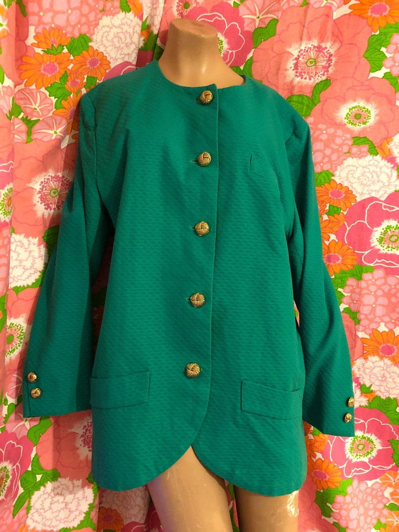 May include: A teal green blazer with a round neckline and gold buttons. The blazer has a textured fabric and two pockets.