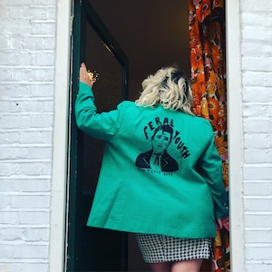 May include: A teal green blazer with a black and white graphic print on the back. The graphic features a person's face with the text "Feral Youth The Teddy Boys".