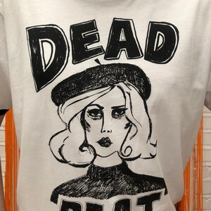 May include: White t-shirt with a black and white illustration of a woman wearing a beret and the text "DEAD BEAT" printed on it.