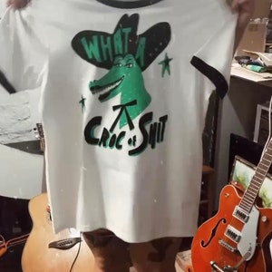 May include: White t-shirt with a green alligator wearing a cowboy hat and the text "What a Croc of Shit".