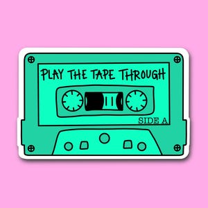 Könnte beinhalten: Türkisfarbener Kassettenband-Aufkleber mit dem Text "PLAY THE TAPE THROUGH" und "SIDE A" in Schwarz. Das Kassettenband-Design hat schwarze Details und einen weißen Rand, vor einem rosa Hintergrund.