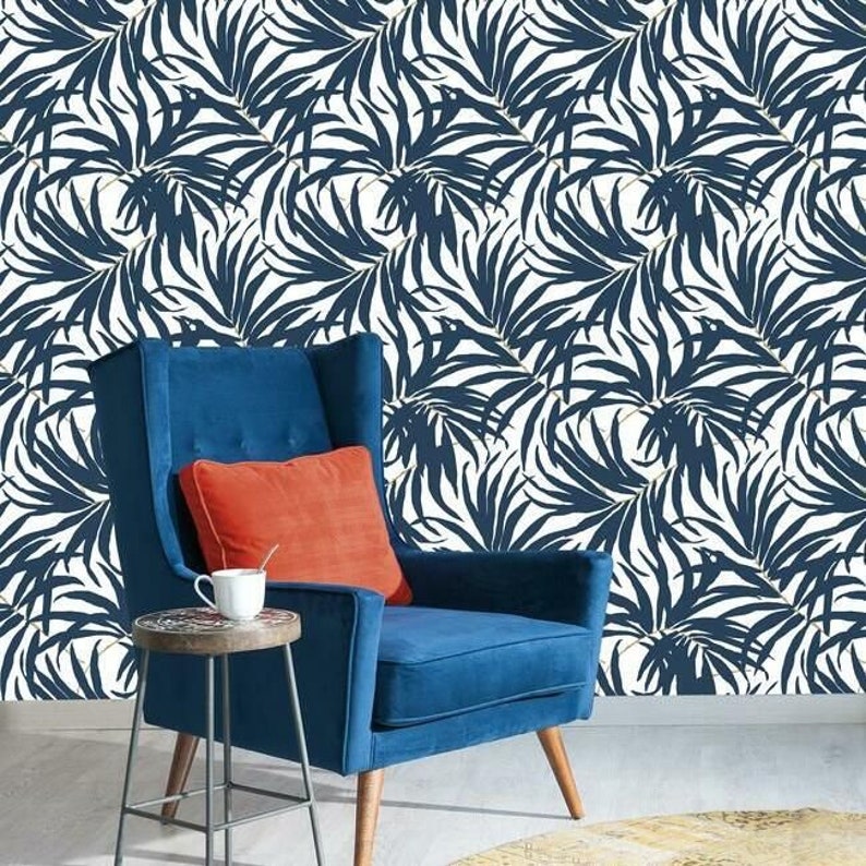 Pu&ograve; includere: Una poltrona blu con un cuscino arancione e un tavolino con una tazza e un piattino. Lo sfondo &egrave; una parete bianca con un motivo ripetuto di foglie di palma blu navy.