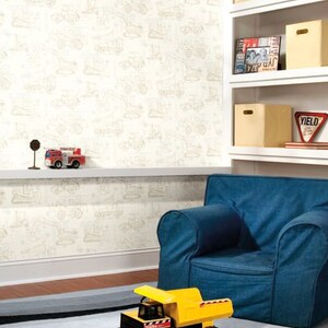May include: A white wallpaper with a pattern of construction vehicles in beige. A blue armchair sits in front of the wallpaper. A yellow toy dump truck sits on a black and gray striped rug.