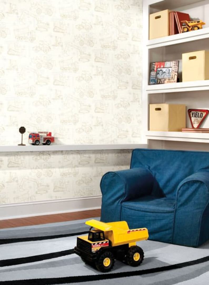 May include: A white wallpaper with a pattern of construction vehicles in beige. A blue armchair sits in front of the wallpaper. A yellow toy dump truck sits on a black and gray striped rug.