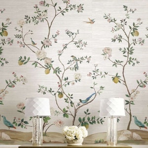 K&ouml;nnte beinhalten: Eine wei&szlig;e Tapete mit einem floralen Muster, das ein sich wiederholendes Design aus &Auml;sten mit rosa Bl&uuml;ten, gr&uuml;nen Bl&auml;ttern und gelben Zitronen zeigt. Zwei wei&szlig;e Lampen mit geometrischen Schirmen stehen vor der Tapete.
