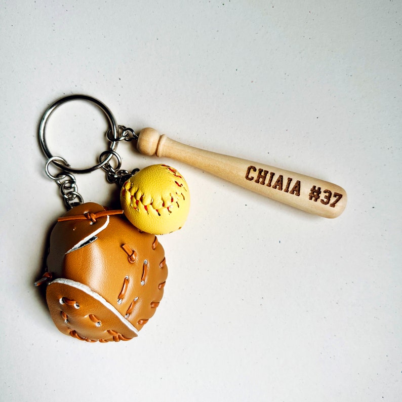 May include: A brown leather baseball mitt keychain with a yellow softball and a wooden baseball bat with the name "CHIAIA #37" engraved on it.
