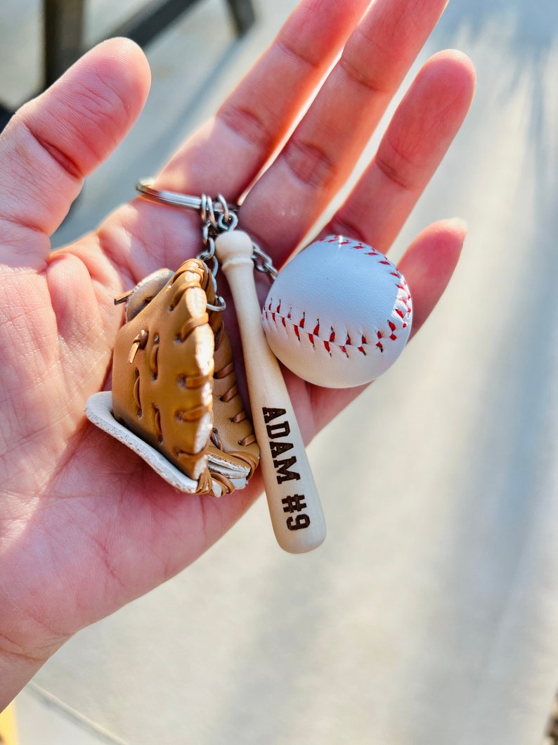 May include: A baseball-themed keychain with a miniature baseball, glove, and bat. The bat is engraved with "ADAM #9".