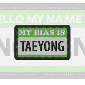 May include: A rectangular embroidered patch with a black border. The patch features a bright green background with the white embroidered text MY BIAS IS above a light gray rectangular section containing the black embroidered text TAEYONG.