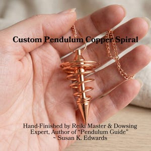 May include: A copper spiral pendulum with a chain, held in a hand. The text on the image reads "Custom Pendulum Copper Spiral" and "Hand-Finished by Reiki Master & Dowsing Expert, Author of 'Pendulum Guide' ~ Susan K. Edwards."