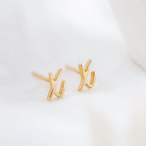 K&ouml;nnte beinhalten: Ein Paar goldfarbene Ohrstecker mit einem einfachen, abstrakten Design. Die Ohrringe sind klein und zart, was sie zu einem dezenten und stilvollen Accessoire macht.