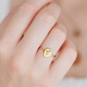 May include: A gold ring with an oval-shaped band featuring a delicate engraved floral design.