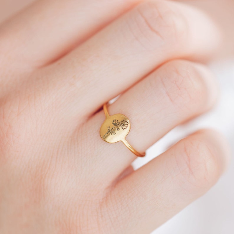 May include: A gold ring with a delicate floral design on the face of the ring. The ring is on a person's finger.