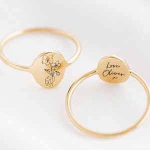 May include: Two gold rings with a floral design on one side and the words "Love Oliver x" engraved on the other side.