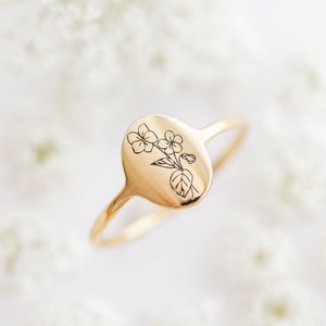 May include: A gold ring with a delicate floral design engraved on the oval band.