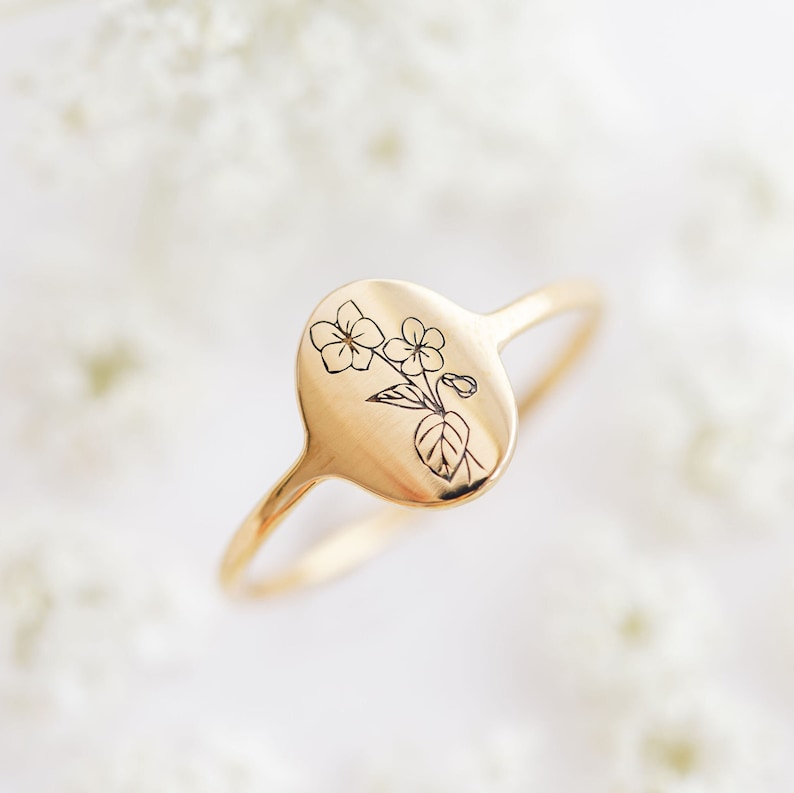 May include: A gold ring with a delicate floral design engraved on the oval band.