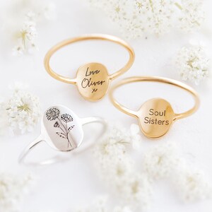 May include: Two gold rings with oval-shaped engraved plates. One ring says "Love Oliver x" and the other says "Soul Sisters". A silver ring with an engraved floral design is also shown.