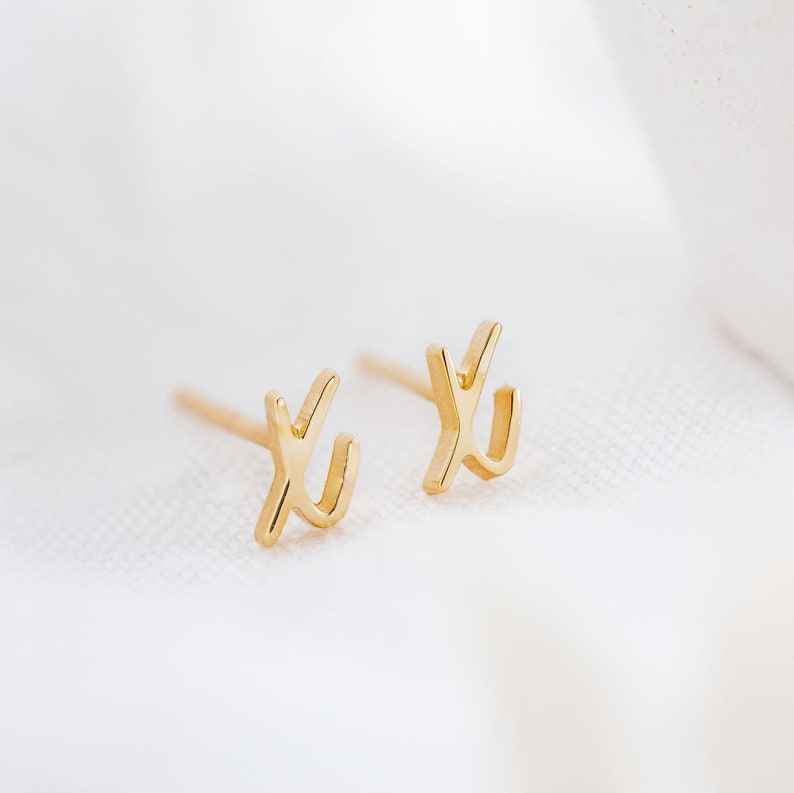 K&ouml;nnte beinhalten: Ein Paar goldfarbene Ohrstecker mit einem einfachen, abstrakten Design. Die Ohrringe sind klein und zart, was sie zu einem dezenten und stilvollen Accessoire macht.