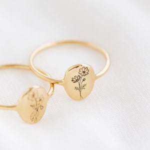 May include: Two gold rings with delicate floral designs engraved on the front. The rings are stacked on top of each other.