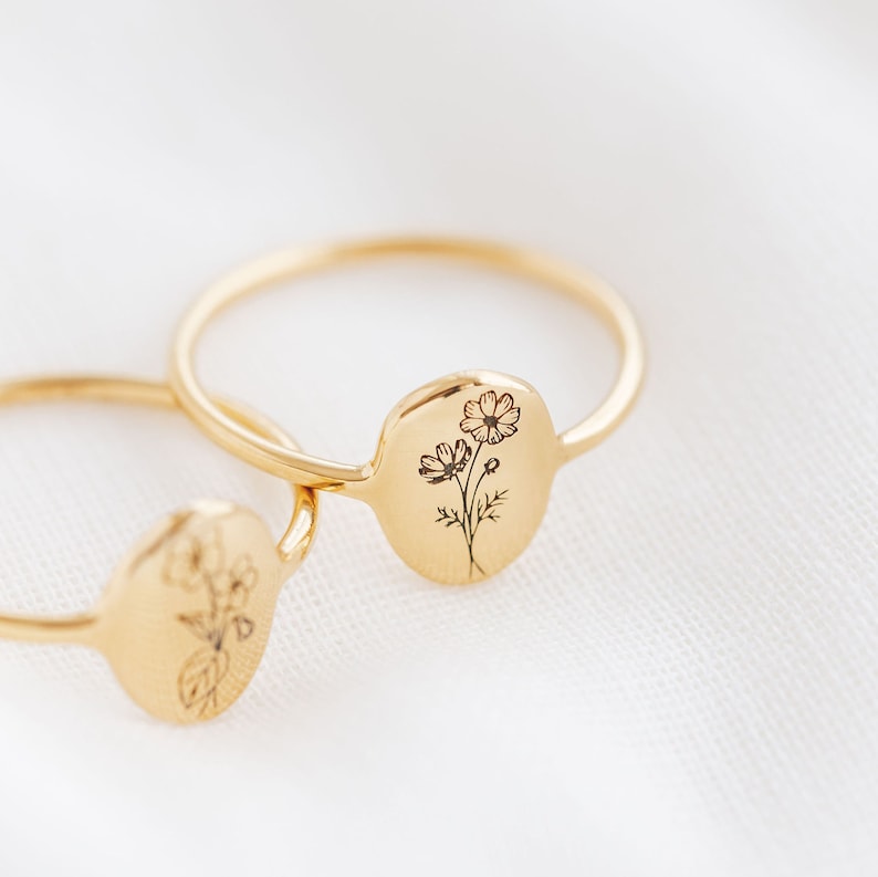 May include: Two gold rings with delicate floral designs engraved on the front. The rings are stacked on top of each other.