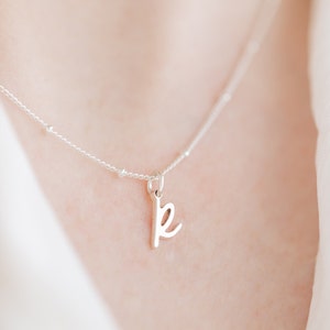 May include: A silver necklace with a delicate chain and a small cursive letter 'k' pendant.