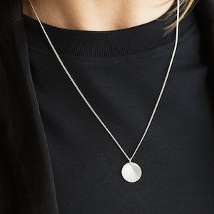 May include: A silver chain necklace with a silver pendant shaped like a seashell. The pendant has a textured surface.